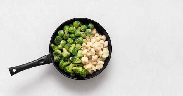 Frozen vegetables in a frying pan on a white background. Cabbage mix. Broccoli, cauliflower, Brussels sprouts. Copy space, top view, flat lay.