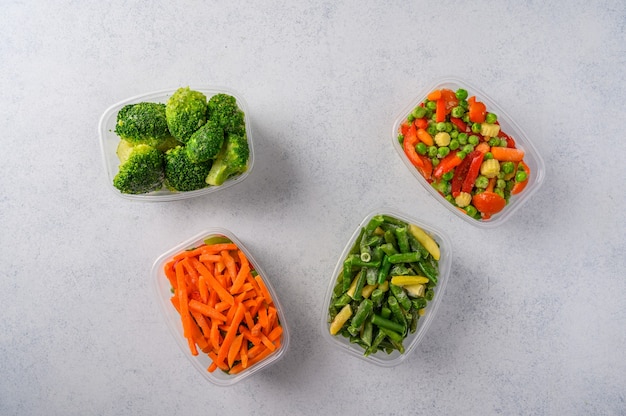 Frozen vegetables mix carrot broccoli spinach green pods beans in plastic trays on light surface