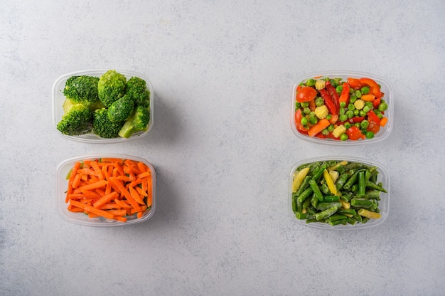 Frozen vegetables mix carrot broccoli spinach green pods beans in plastic trays on light surface