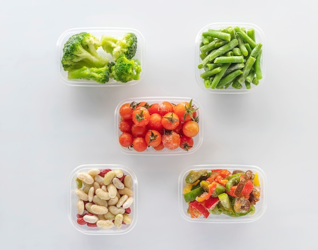 Frozen vegetables in plastic containers on white background. Flat lay. Frozen broccoli, green beans, cherry tomatoes, beans and bell pepper.