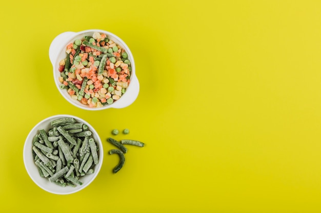 Frozen vegetables: string beans and a mix of vegetables in white bowls on a bright yellow background.