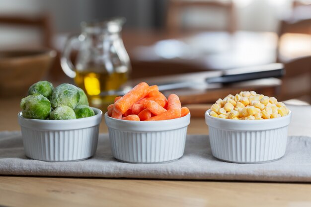 Photo frozen vegetables such as baby carrot and and brussels sprouts in the bowls on the kitchen table, horizontal