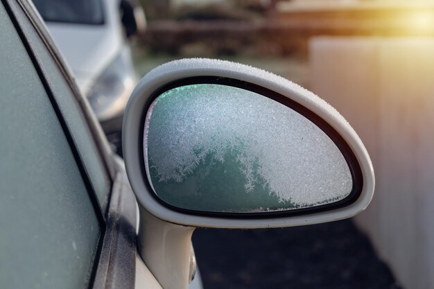 Frozen white rearview mirror of a parked car in a outdoor parking early winter frost