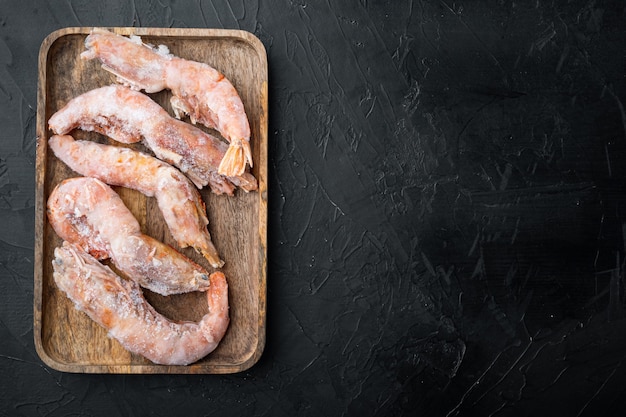 Frozen wild Argentinian red shrimps with heads set, on wooden tray, on black