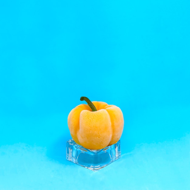 Frozen yellow pepper on ice cube on blue background