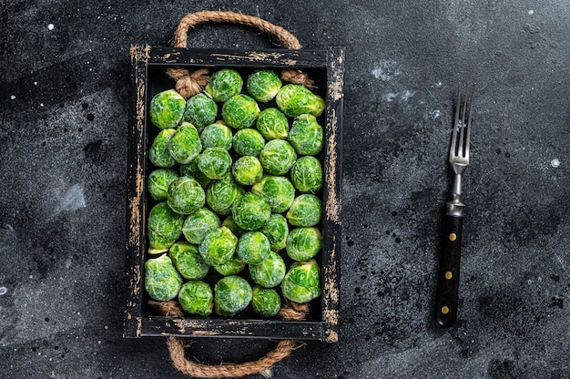 Photo frozen young brussels sprouts green cabbage in wooden tray. black background. top view.