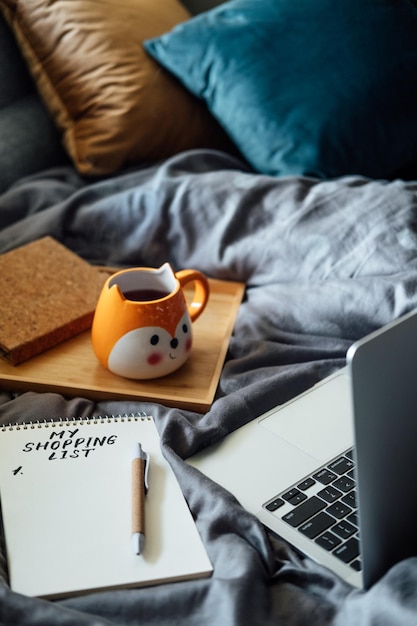 Frugal living tips save money concept with shopping list in notebook near laptop and tea coffee cup