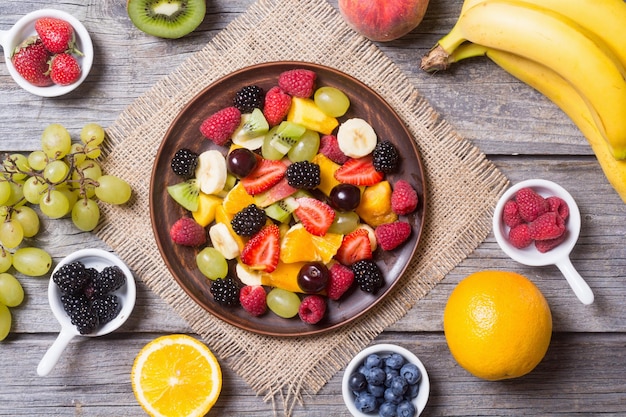 Фото Салат из фруктов и ягод в керамической тарелке на деревянном фоне, вид сверху