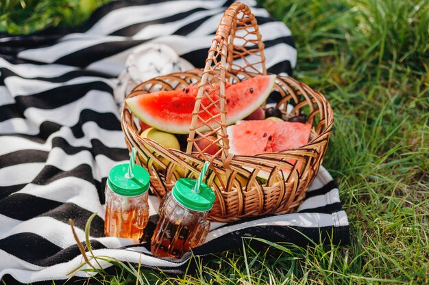 Корзина с фруктами и бокалы с напитком на пикнике на свежем воздухе