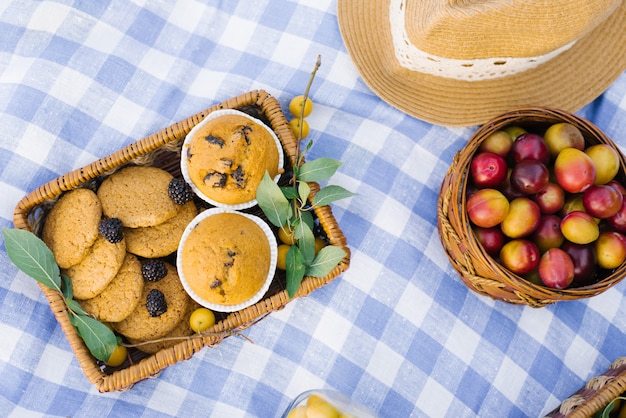 Frutta e bacche in cestini da picnic su un bianco blu controllato tovaglia su un prato verde e un cappello di paglia