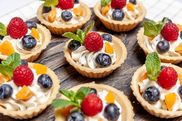 Fruit and berry tartlets dessert assorted on wooden tray.\
closeup of delicious pastry sweets pies colorful cakes with fresh\
natural raspberry blueberry and cheese cream. french bakery\
catering.