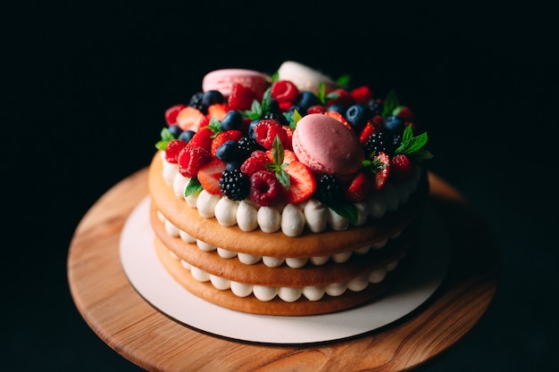 Фруктовый торт торт украшен ягодами на деревянной подставке на черном.