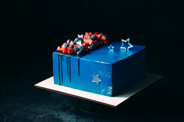 Fruit cake. Cake decorated with berries on a wooden stand on a black 