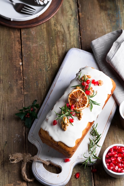 Fruit cake dusted with icing, nuts, kernels pomegranate and dry orange on old wooden . Christmas and Winter Holidays homemade cake