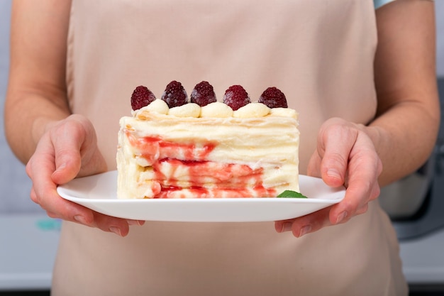 Fruit cake on saucer in female hands. Close up. Piece of pie with berries and cream.
