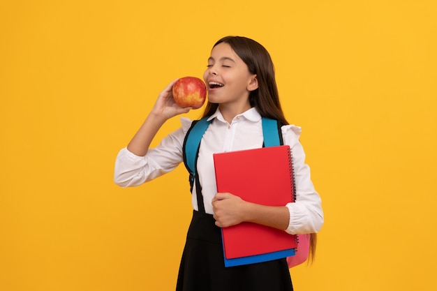 Il frutto dell'educazione è dolce bambino mangia mela in possesso di libri scolastici educazione alimentare spuntino scolastico