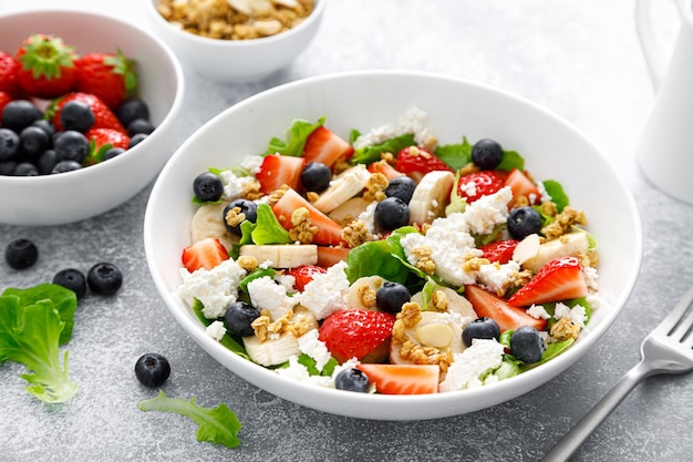 Fruit- en bessensalade met verse aardbeien, bosbessen, bananenkwark en muesli met amandel Gezond voedseldieetontbijt