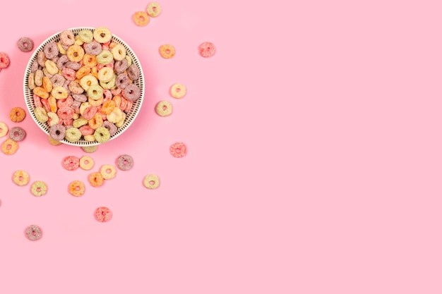 Fruit flavor colored cereals in a bowl on a pink background with copy space