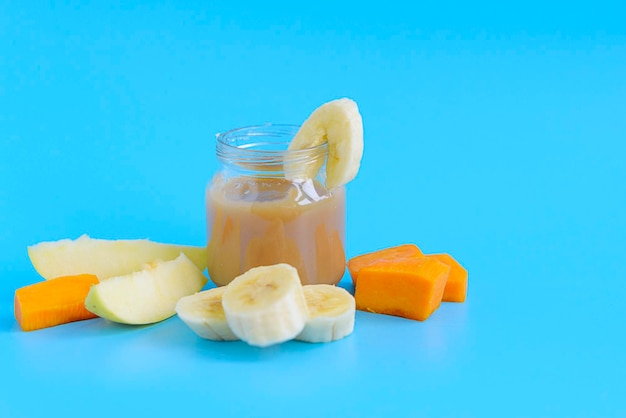 Fruit handmade baby food with apples, bananas, pears and pumpkin in glass jars on a blue background, copy space healthy food for children