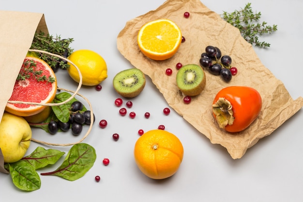 Fruit in papieren zak. Dadelpruim, kiwi en sinaasappel op papier. Snijbiet bladeren en veenbessen op tafel.