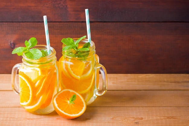 オレンジフルーツレモンミントの水木製の板の上にあるメイソンの瓶に氷の夏の飲み物