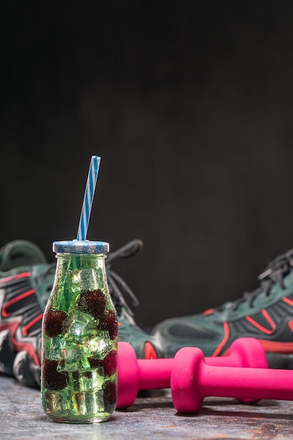 Foto bottiglia d'acqua con infusore di frutta con cannuccia e frutta in acqua vicino a scarpe da ginnastica e manubri