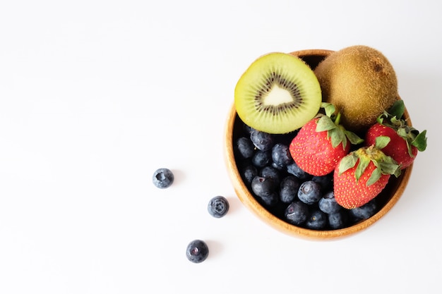 The fruit is placed in a brown wooden bowl on a white table.