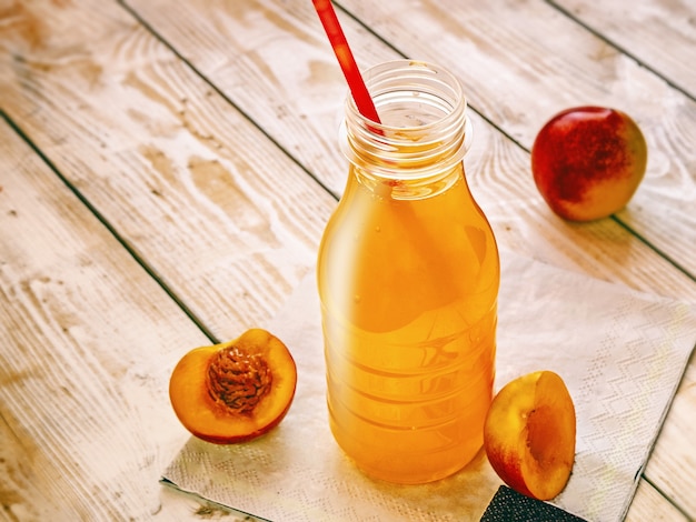 Fruit non-alcoholic drink in a bottle with pieces of nectarine fruit on wood