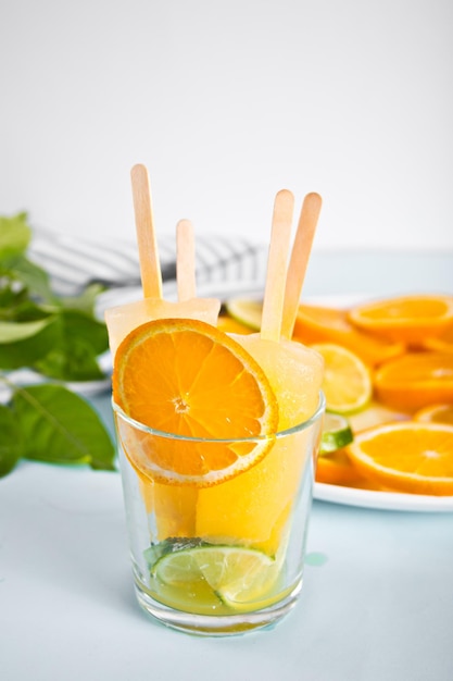 Fruit orange citrus popsicles ice pops in glass and slices of orange on plate on the background