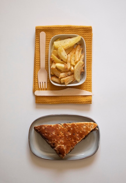 Fruit pastry slice with a plate of french fries and a fork and knife on a white background