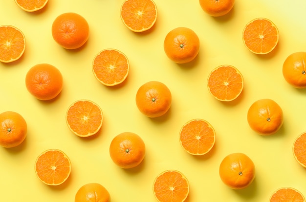 Fruit pattern of fresh orange slices on yellow background. Pop art design, creative summer concept. Half of citrus in minimal flat lay style.