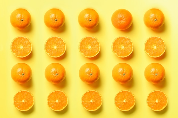 Fruit pattern of fresh orange slices on yellow background. Pop art design, creative summer concept. Half of citrus in minimal flat lay style.