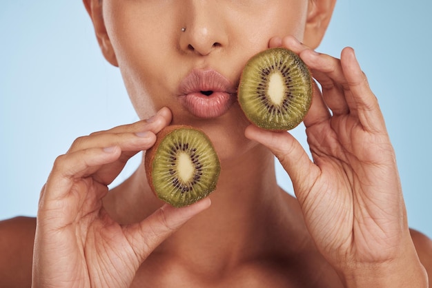 Fruit pout and woman with kiwi for skincare or organic dermatology treatment isolated in a blue studio background Skin beauty and young female person with facial wellness nutrition and detox