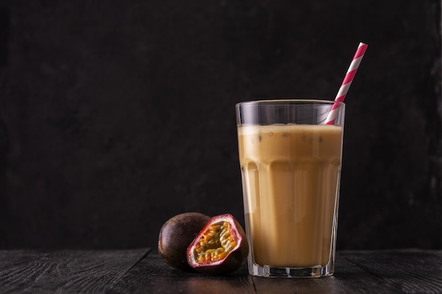 Fruit protein shake on a black wooden background. Fresh milkshake with passion fruit. A glass of protein shake.