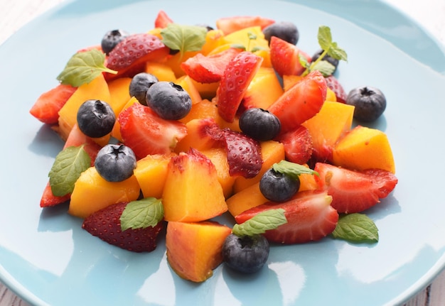 흰색 배경에 파란색 접시에 있는 과일 샐러드 얇게 썬 딸기 복숭아와 민트 잎이 있는 블루베리 텍스트를 위한 여유 공간