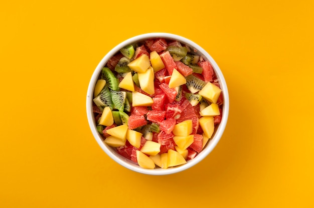 Fruit salad bowl on yellow background top view Diet food concept