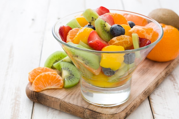 Fruit salad in crystal bowl on white wooden table.