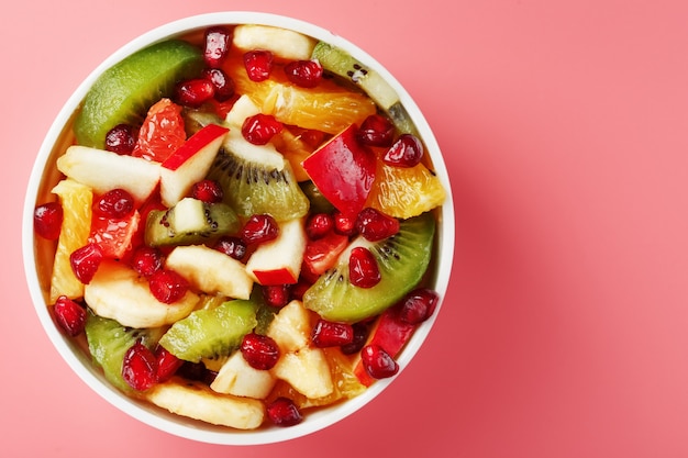 Fruit salad in a cup on a pink table. Slices of fresh, juicy and healthy fruits