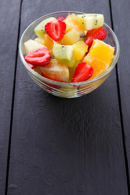 Fruit salad from pineapple kiwi orange and strawberry on black background Multicolored sliced fruits in transparent bowl Copy space