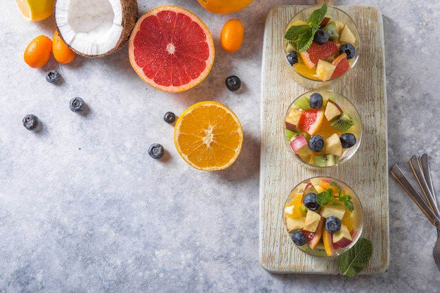 Insalata di frutta in bicchieri, cibi freschi d'estate, mirtilli di kiwi arancioni biologici sani, ananas, cocco. vista dall'alto