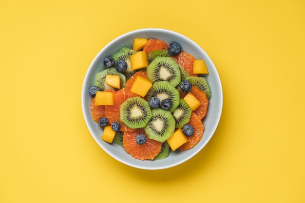 Fruit salad of red oranges, kiwi, mango and berries isolated on yellow background