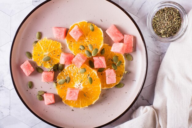 Fruit salad of watermelon orange and pumpkin seeds on a plate Healthy food Top view Closeup