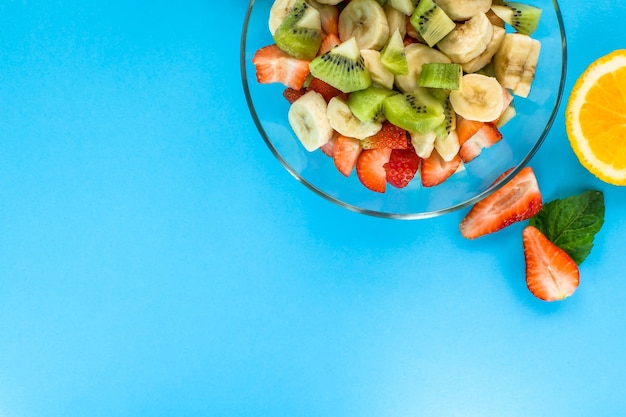 Fruit salad with strawberry kiwi orange and lemon on wooden background Top view with copy space