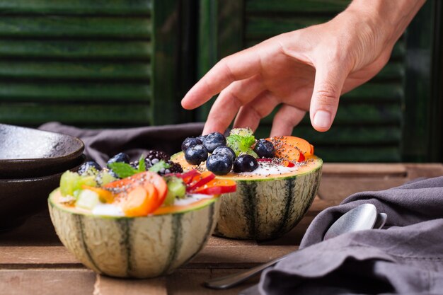 Fruit salad with yogurt in carved melon cantaloupe bowl on table