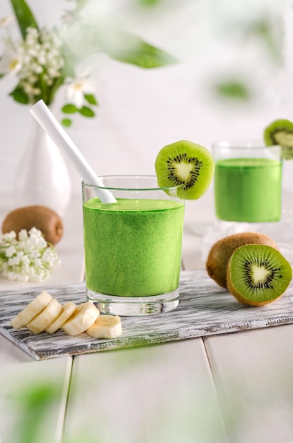 Fruit smoothie with kiwi and banana on a white wooden table in a glass cup.