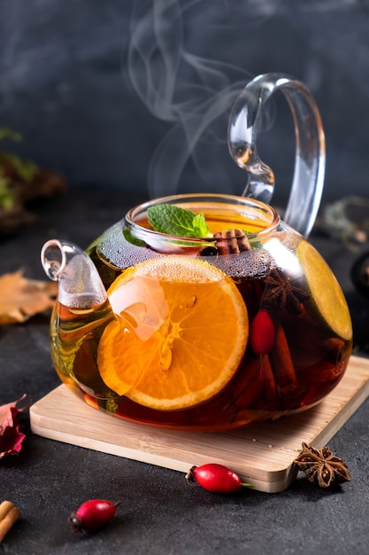 Fruit tea. Seasonal winter autumn hot drink. Citrus and berry tea with lemon, oranges in glass teapot on dark  table