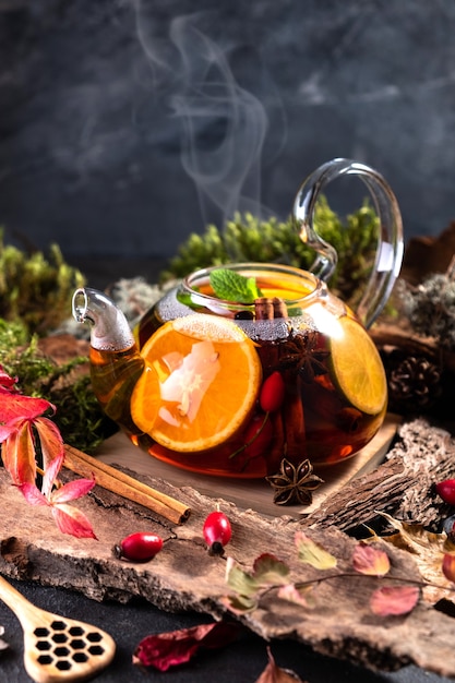 Fruit tea. Seasonal winter autumn hot drink. Citrus and berry tea with lemon, oranges in glass teapot on dark  table