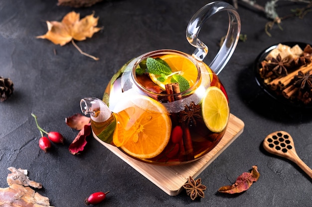 Fruit tea. Seasonal winter autumn hot drink. Citrus and berry tea with lemon, oranges  and mint in glass teapot on dark  table