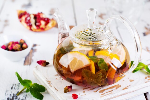 Fruit tea with berries, lemon, lime and mint leaves in glass teapot