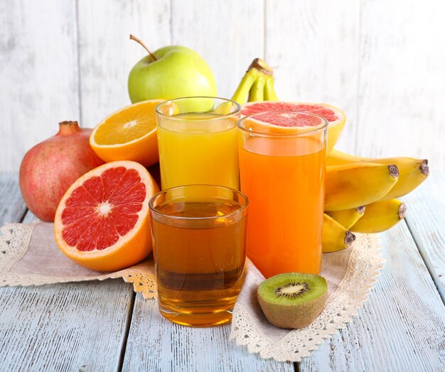 Fruit and vegetable juice and fresh fruits on napkin on wooden table on wooden wall background